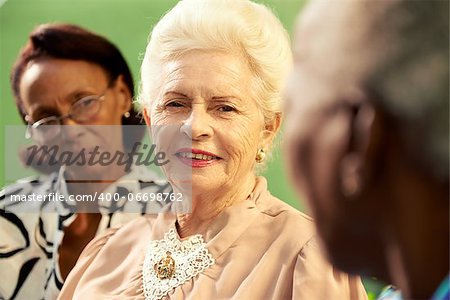 Active retired elderly women and free time, group of happy senior african american and caucasian female friends talking and sitting on bench in park