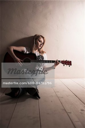 Young Woman Sitting on the Floor Playing Guitar in Studio