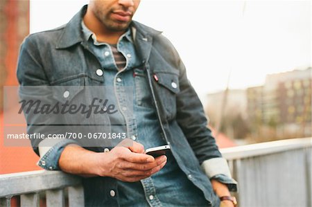 Close-up of young man texting on an iPhone in an urban setting. Close-up of young man texting on an iPhone in an urban setting.