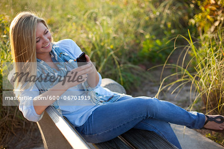 Young Woman Sitting on Bench at Beach, Texting on Cell Phone, Jupiter, Palm Beach County, Florida, USA