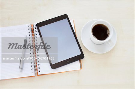 still life of a tablet pc, notebook, pen, and a cup of coffee