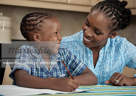 Young African child doing her homework while being helped by her mother
