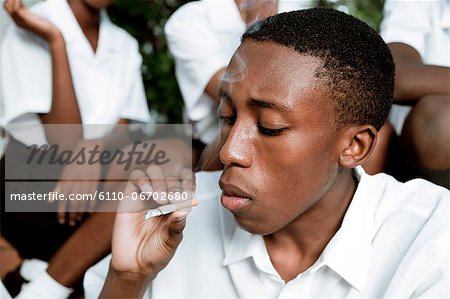 An African teenage boy sitting outside smoking a cigarette