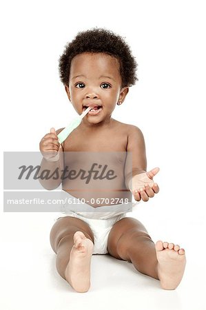 An infant sitting in front of a white background, smiling