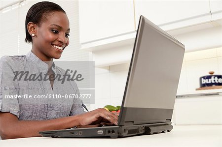 Young African woman working on a laptop in the kitchen, smiling