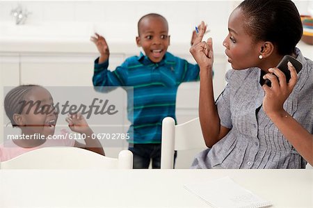 Young African mother trying to talk on her cellphone while her children play in the background