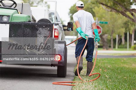 Pest control technician with high pressure spray gun and hose at his truck