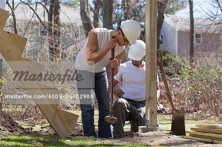 Hispanic carpenters using sledge hammer to tamp dirt at deck footing