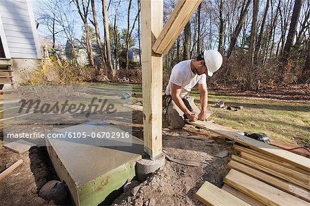 Hispanic carpenter marking deck flooring for corner cuts for installation