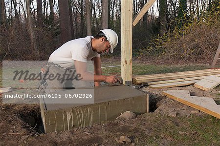 Hispanic carpenter putting smooth edge on stairway footing concrete
