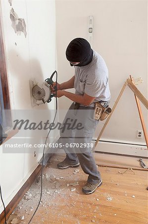 Hispanic carpenter using circular saw to cut wallboard for deck doorway in house