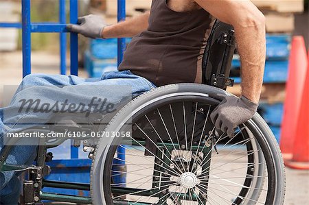 Loading dock worker with spinal cord injury in a wheelchair moving a hand truck