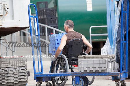 Loading dock worker with spinal cord injury in a wheelchair moving stacked inventory trays