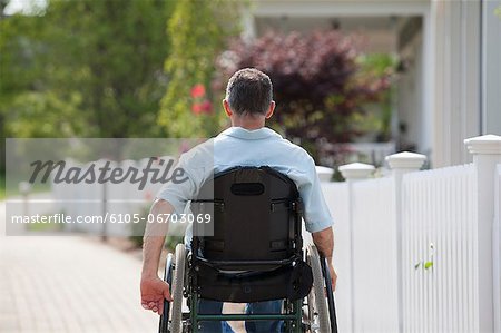 Man with spinal cord injury in a wheelchair on a suburb walk with homes