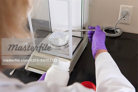 Laboratory scientist adding a small amount of solid reagent to a container on a scale