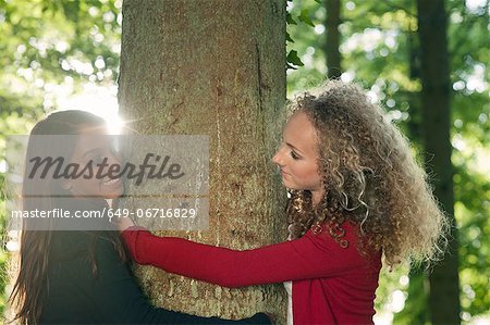 Teenage girls hugging tree in forest
