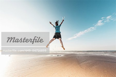 Woman jumping with light bulb on beach