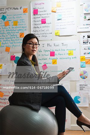 Woman sitting on exercise ball with digital tablet