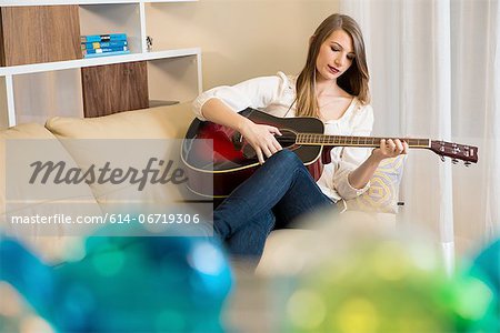 Woman playing guitar on sofa