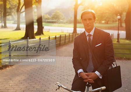 Businessman sitting on bicycle in urban park