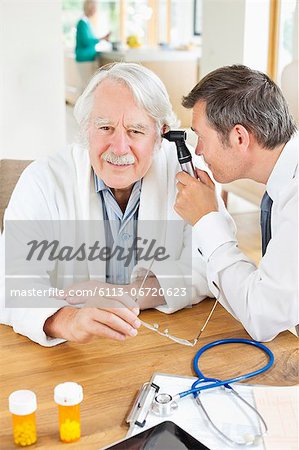 Doctor examining older man's ear at house call