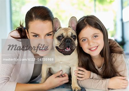 Smiling mother and daughter hugging dog
