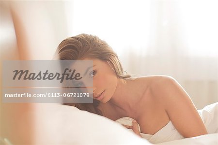 Nude woman wrapped in sheet on bed