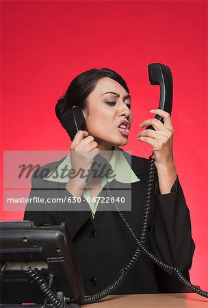 Businesswoman using multiple landline phones and shouting