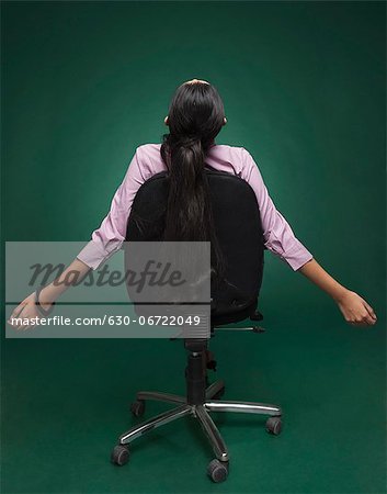 Rear view of a businesswoman sitting on a chair with her arm outstretched