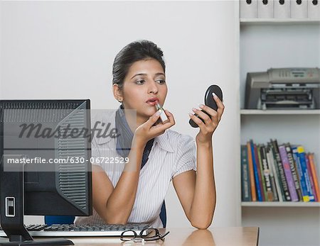 Businesswoman applying lipstick in an office
