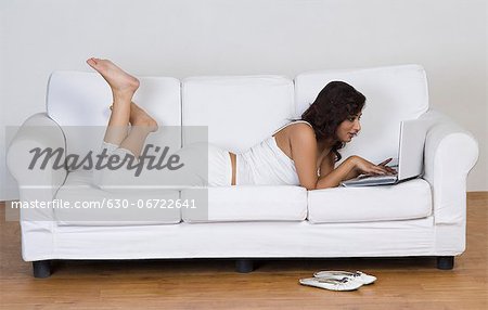 Woman lying on a couch and using a laptop