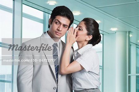 Businesswoman whispering to a businessman