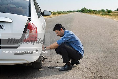 Businessman changing the punctured tire of his car