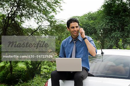 Businessman using a laptop and a mobile phone while sitting on his car
