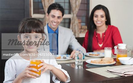 Portrait of a girl holding a glass of juice with her parents in the background