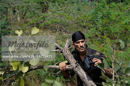 Soldier holding binoculars in a forest