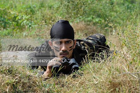 Soldier lying in a forest with binoculars