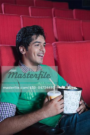Close-up of a man enjoying movie with popcorns and soft drink in a cinema hall