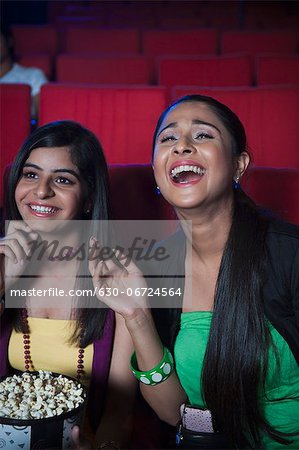 Two female friends enjoying movie with popcorns in a cinema hall