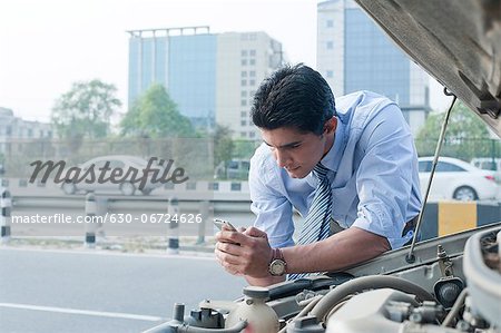 Businessman leaning on a broken down car and using mobile phone, Gurgaon, Haryana, India