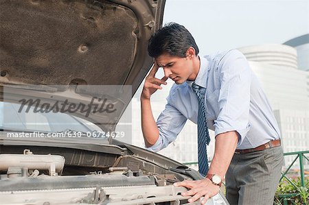 Businessman examining his broken down car, Gurgaon, Haryana, India