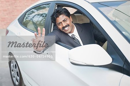 South Indian businessman driving the car and waving hand