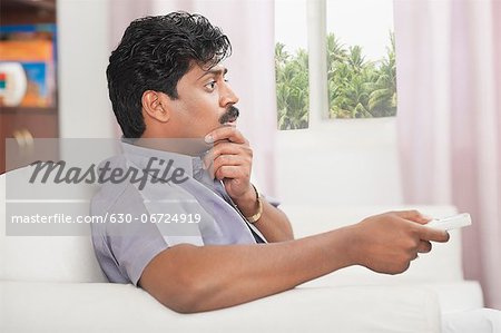 South Indian man watching TV and looking surprised