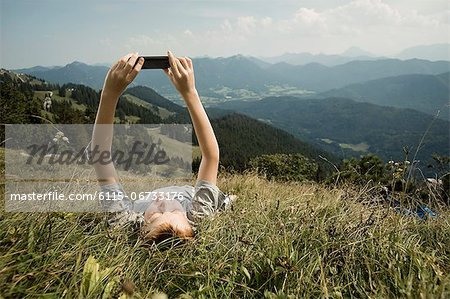 Germany, Bavaria, Boy lying on back in mountains uses a smart phone