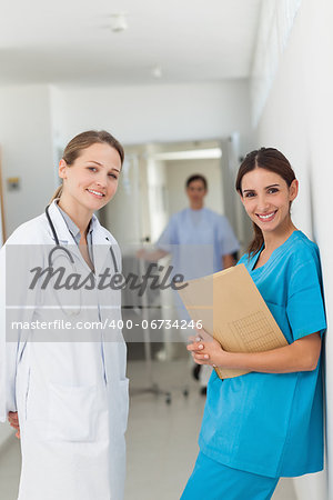 Doctor and a nurse against a wall standing side by side in a hallway in a hospital