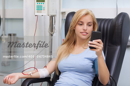 Blood donor looking at her mobile phone in hospital ward