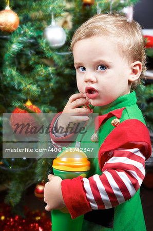 One year old baby boy by the Christmas tree, dressed as an elf.