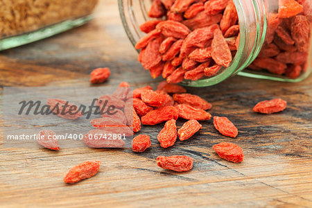 Tibetan goji berries (wolfberry) spilling of the glass jar on a wooden surface, selective focus