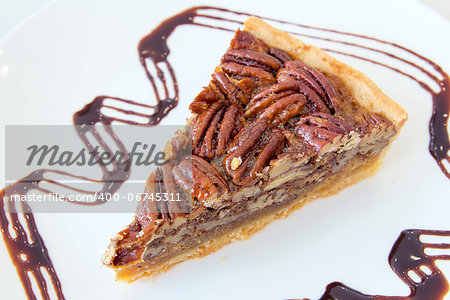 Pecan Nuts Pie with Slice with Dark Chocolate Drizzle on White Plate Closeup