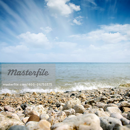 coast stones and sea wave over cloudy sky in summer - shallow DOF with focus on stones